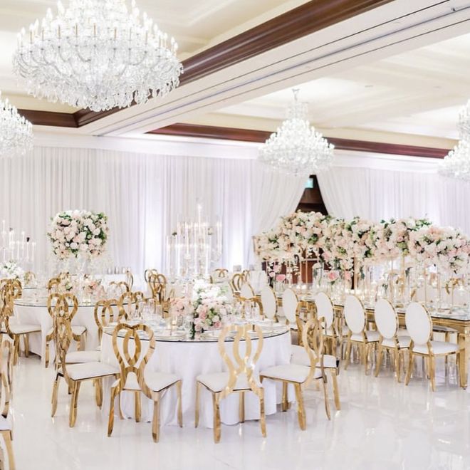 ديكور قاعة زفاف فاخرة بطاولات مستديرة وكراسي ذهبية
وزهور وردية وثريات كريستال يوضح شكل القاعة عند تجهيز الضيافة لحفل
زواج راقٍ في السعودية