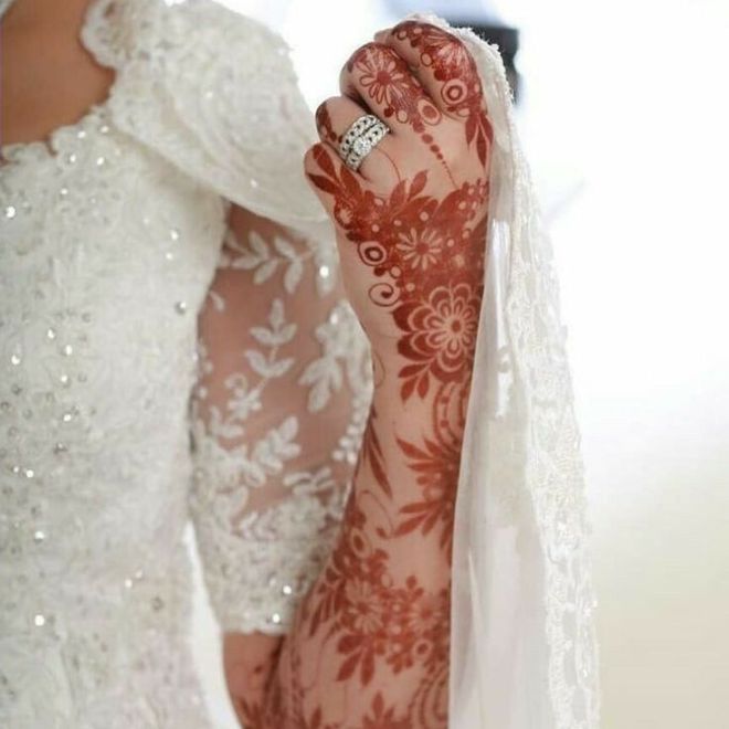 نقش حناء بني يغطي ذراع عروس ترتدي فستان زفاف أبيض مزخرف
بالدانتيل