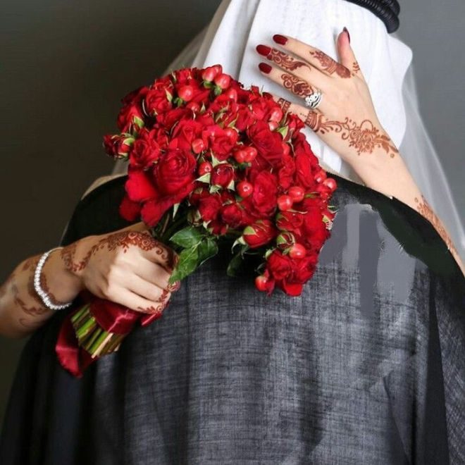 عروس سعودية بنقش حناء تمسك باقة ورد حمراء وتحتضن عريساً
يرتدي البشت في يوم الزفاف