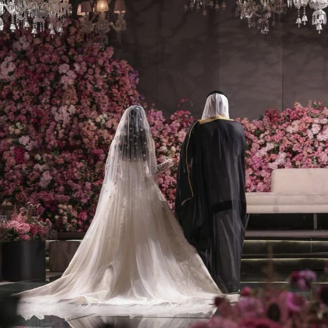 منصة زفاف سعودية مزينة بالزهور والثريات، العروس والعريس
من الخلف في لقطة احتفالية أنيقة بعد إتمام التحضيرات